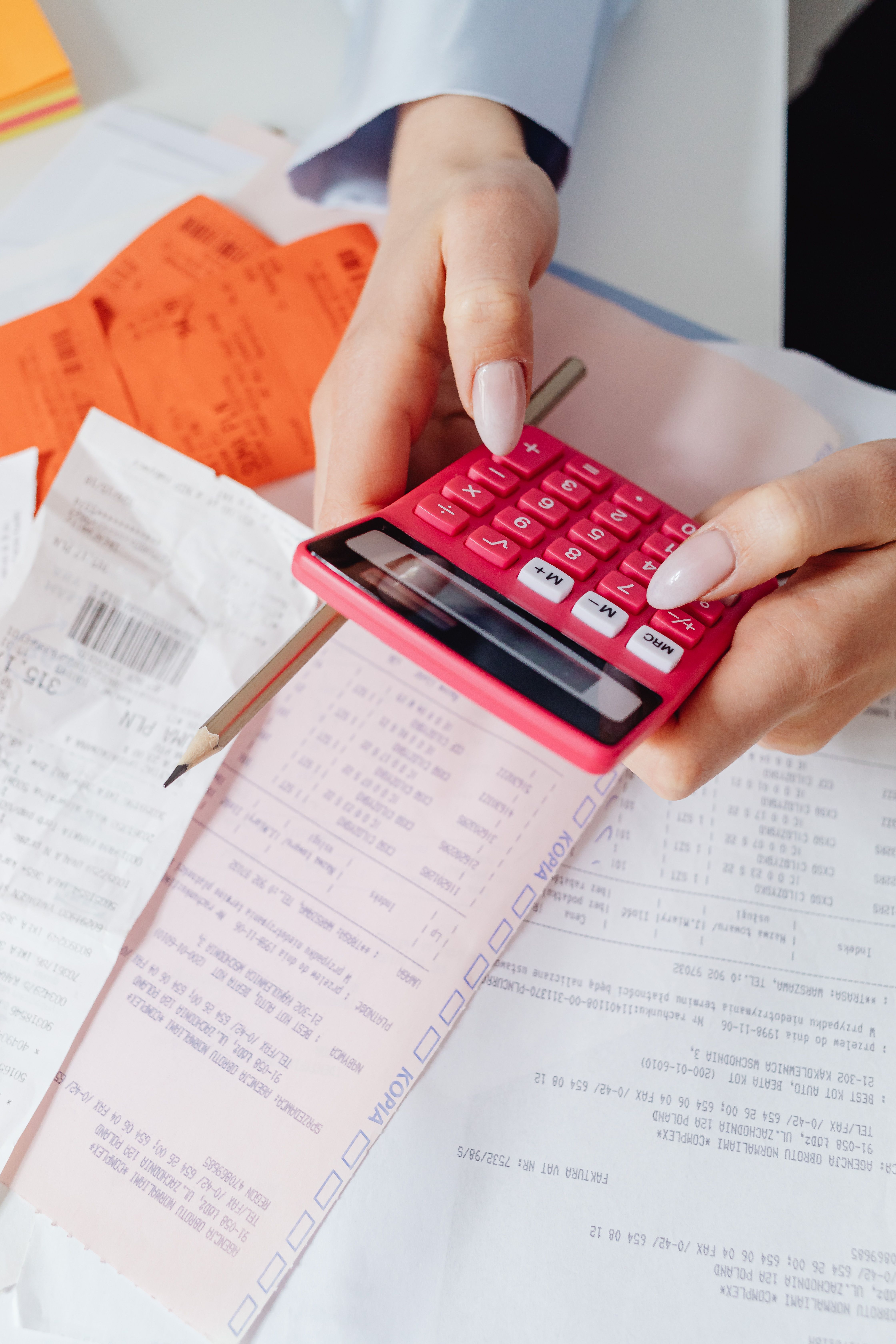 Person using a bright pink calculator on top of receipts and invoices, with a pencil nearby.